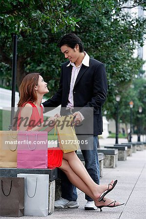 Woman sitting on park bench, looking at man standing next to her