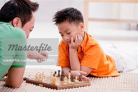 Vater und Sohn auf Boden, liegend spielt Schach