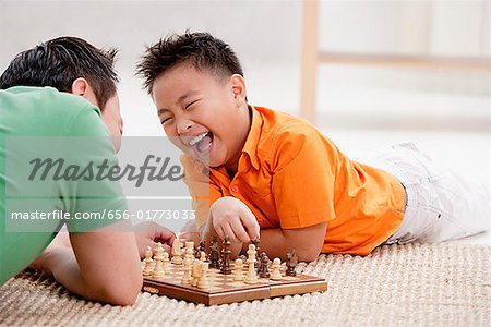 Father and son lying on floor, playing chess, laughing