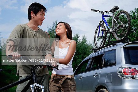 Homme sur une moto, femme debout à côté de lui, le véhicule utilitaire sport en arrière-plan