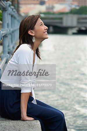 Woman sitting by river, smiling, looking up