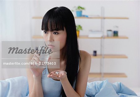 Young woman holding glass of water and pills, looking away