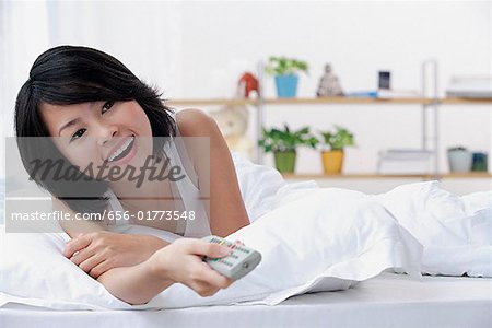 Junge Frau liegend auf dem Bett, mit TV-Fernbedienung