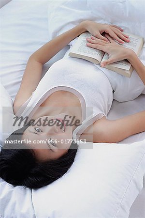 Junge Frau auf dem Bett liegend, mit einem Buch, Blick in die Kamera