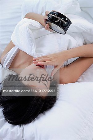 Jeune femme sur le lit, regardant le réveil, la main sur la bouche