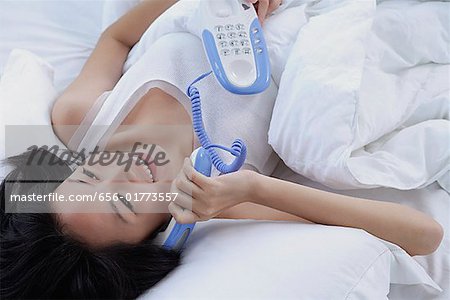 Young woman on bed, using telephone