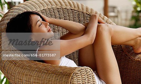 Young woman sitting on wicker chair, eyes closed