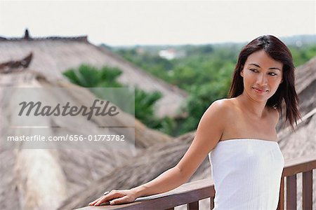 Jeune femme se penchant sur la rampe à la recherche, chaume des toits derrière elle