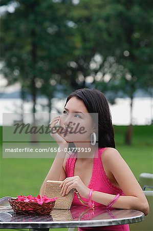 Young woman sitting at outdoor table, hand on chin, looking away