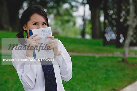 Young woman in school uniform, book covering face