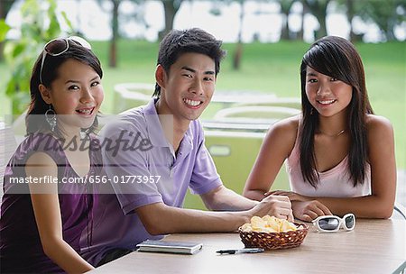 Young adults sitting at outdoor cafe, smiling at camera