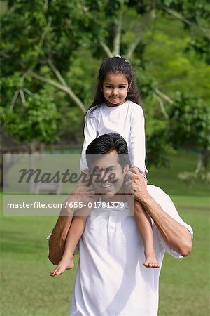 Un père porte sa fille sur ses épaules, car ils ont tous deux regardent la caméra