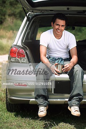 Young man sitting in car boot smiling at camera