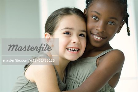 Two young female friends embracing, both smiling at camera