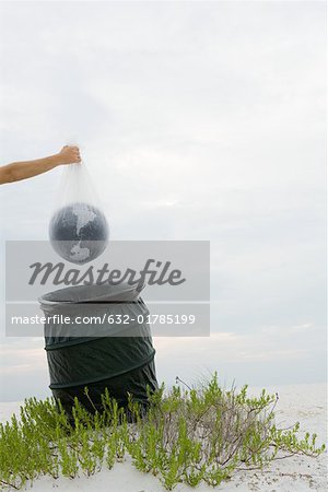 Person holding globe in plastic bag over garbage can, cropped view