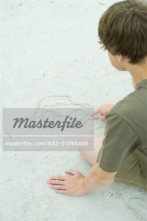 Teen boy drawing car in sand