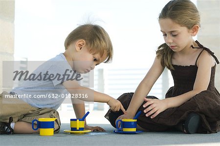 Brother and sister sitting on the ground, playing with plastic cups