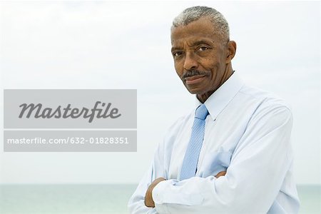 Senior man wearing tie outdoors, arms folded, looking at camera