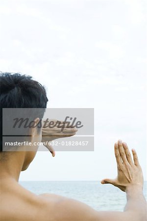 Man looking at sea through finger frame, over the shoulder view