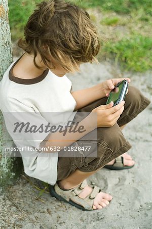 Boy sitting on the ground playing with handheld video game, high angle view