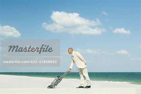 Man in suit using vacuum cleaner on beach, full length