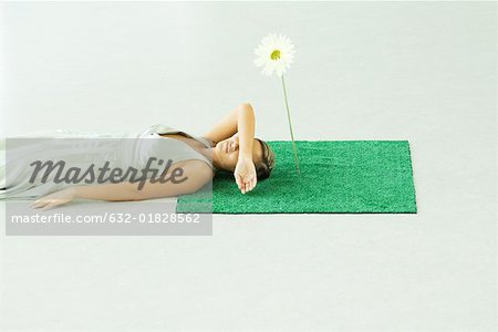 Woman lying with head on square of artificial turf, covering eyes with arm