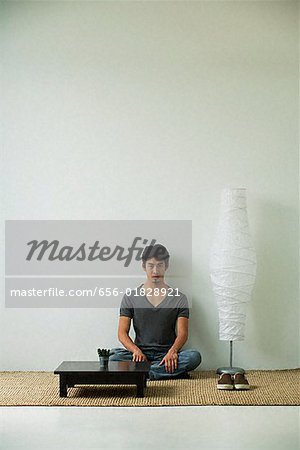 Serious young man sitting on floor, looking at camera