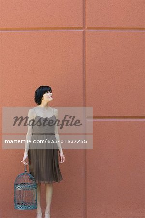 Woman standing, holding emZSy bird cage, looking up