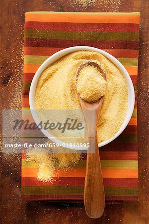 Polenta in bowl with wooden spoon on coloured cloth