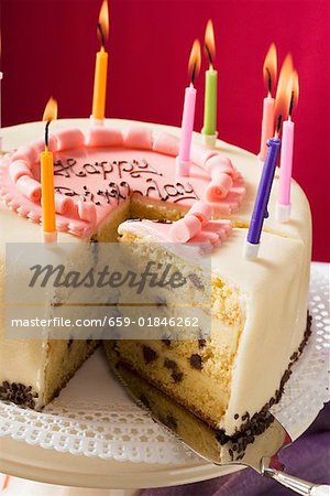 Birthday cake with burning candles, a piece cut