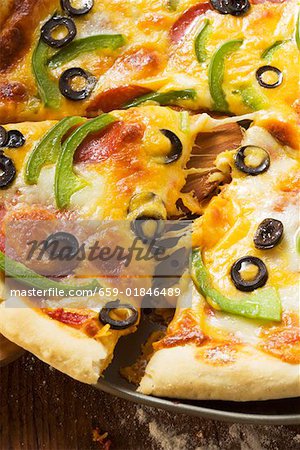 Pizza with cheese, salami, peppers and olives, a piece cut