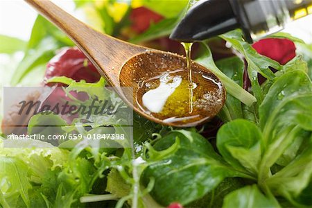 Blätter gießen Öl in hölzernen Löffel über den Salat