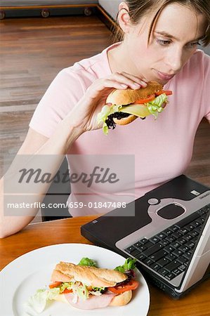 Jeune femme mangeant un sandwich alors qu'il travaillait à l'ordinateur