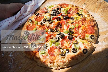 Main tenant la pizza au pepperoni aux poivrons et aux olives