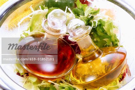 Oil and vinegar bottles lying on green salads