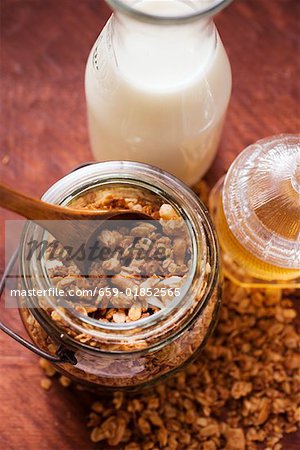 Crunchy muesli in a jar, honey and milk bottle beside it
