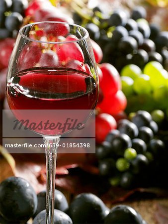 Ein Glas Rotwein mit gemischten Trauben im Hintergrund