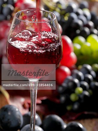 Gießen ein Glas Rotwein mit Trauben im Hintergrund