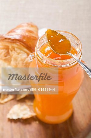 Apricot jam in jar with spoon, croissant