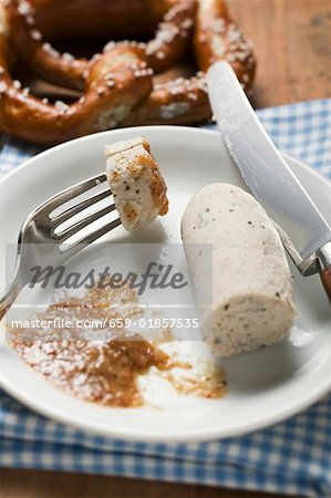 Gekochte Weißwurst mit Senf auf Teller, Brezel hinter