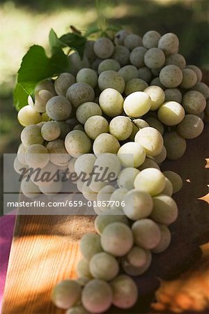 Green grapes with leaves on wooden chopping board