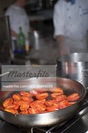 Tomatoes in frying pan on stove, chefs in background
