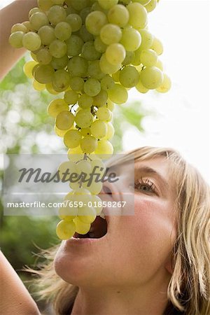 Woman holding fresh green grapes above her mouth