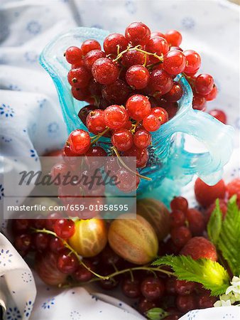 Redcurrants in blue glass jug, surrounded by berries