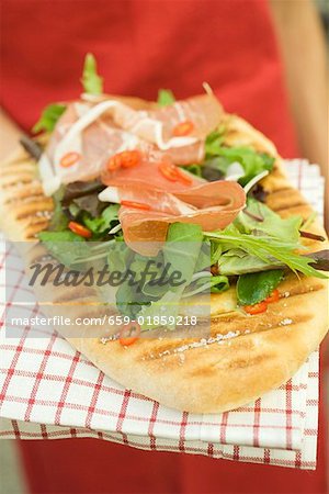 Woman holding pizza bread topped with Parma ham, herbs, chilli rings