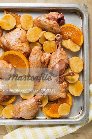 Roast chicken pieces with oranges on baking tray