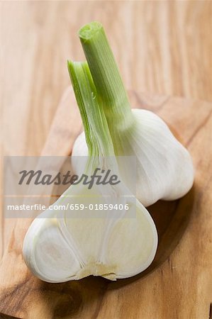Whole and half garlic bulb on wooden chopping board