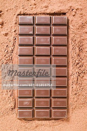 A bar of dark chocolate on cocoa powder
