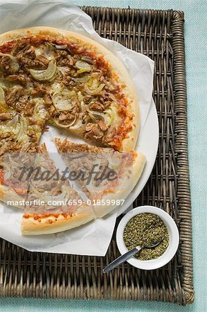 Tuna and onion pizza, partly sliced, oregano beside it