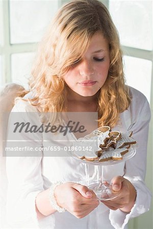 Blond girl holding glass bowl of assorted gingerbread biscuits